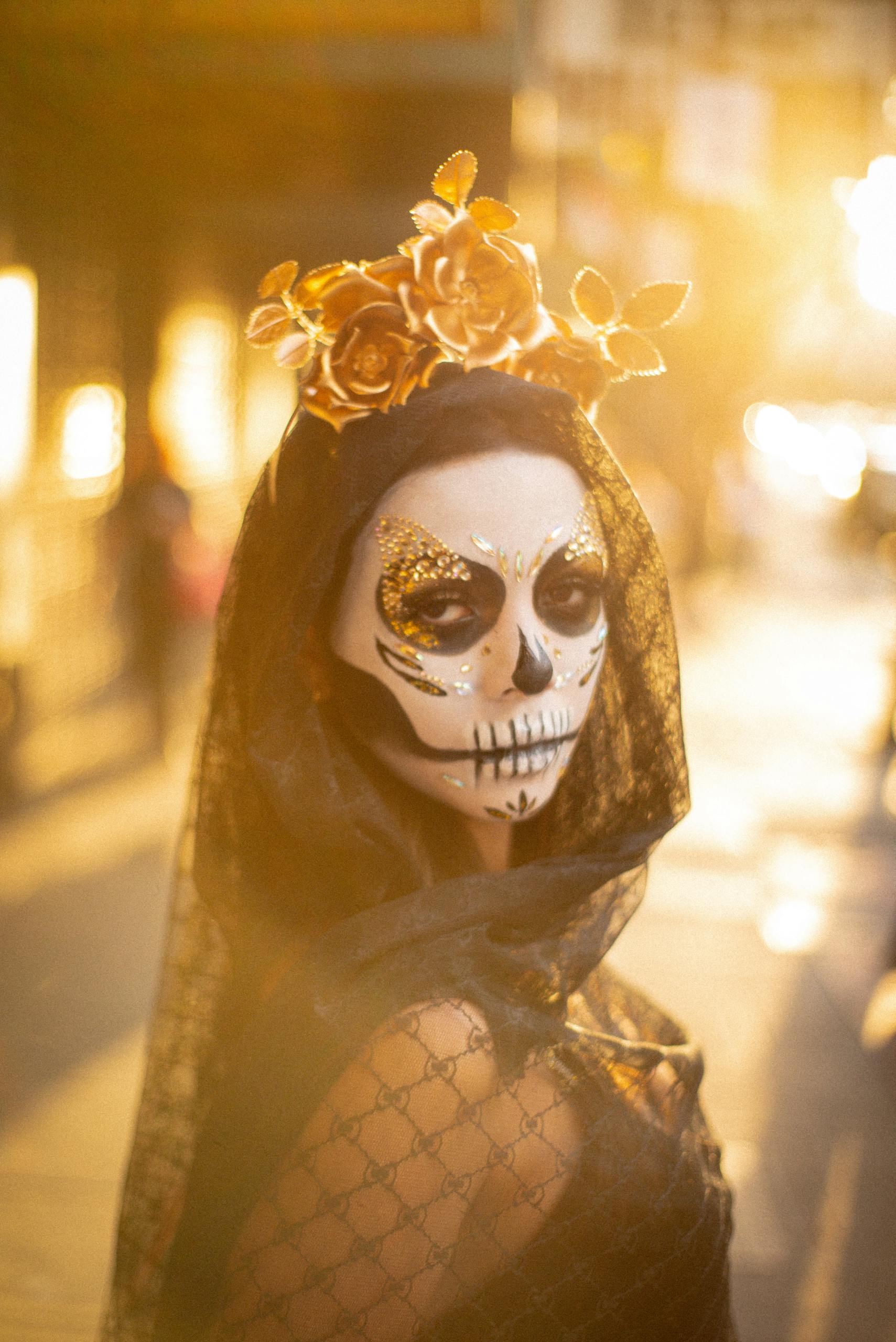 A person wearing Day of the Dead makeup and costume with a golden floral crown in warm sunlight.